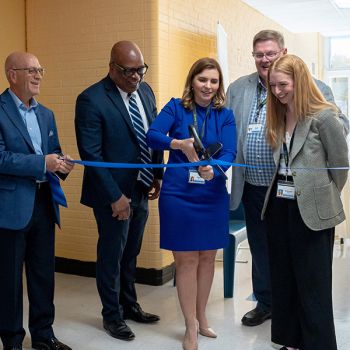 Adelbrook leaders cutting a blue ribbon with large scissors