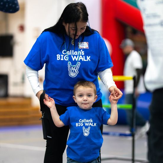 A woman and young boy holding hands and wearing blue t-shirts that say "Callan's BIG WALK"