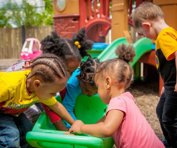 Kids digging in a large green bucket in a playground