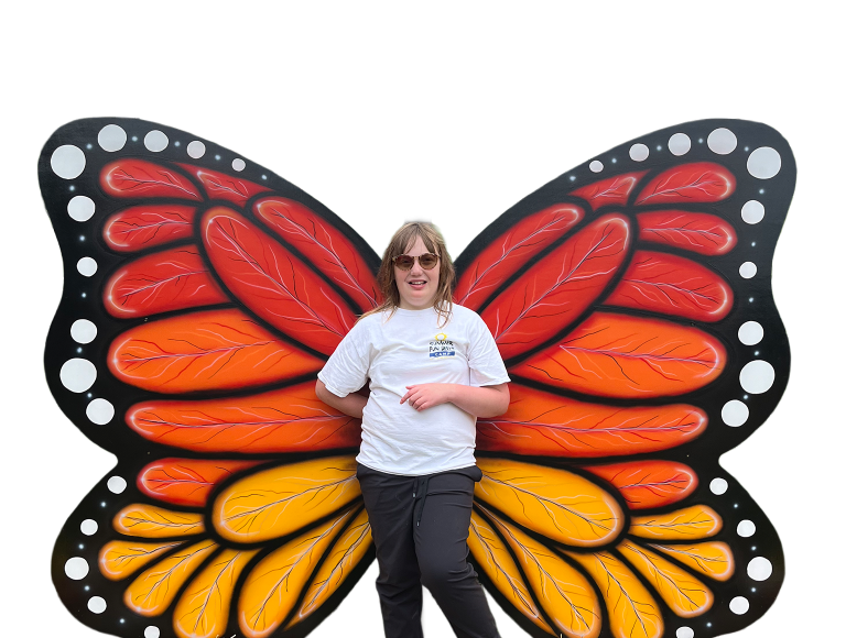 Young girl smiling while standing in front of large wooden monarch butterfly wings